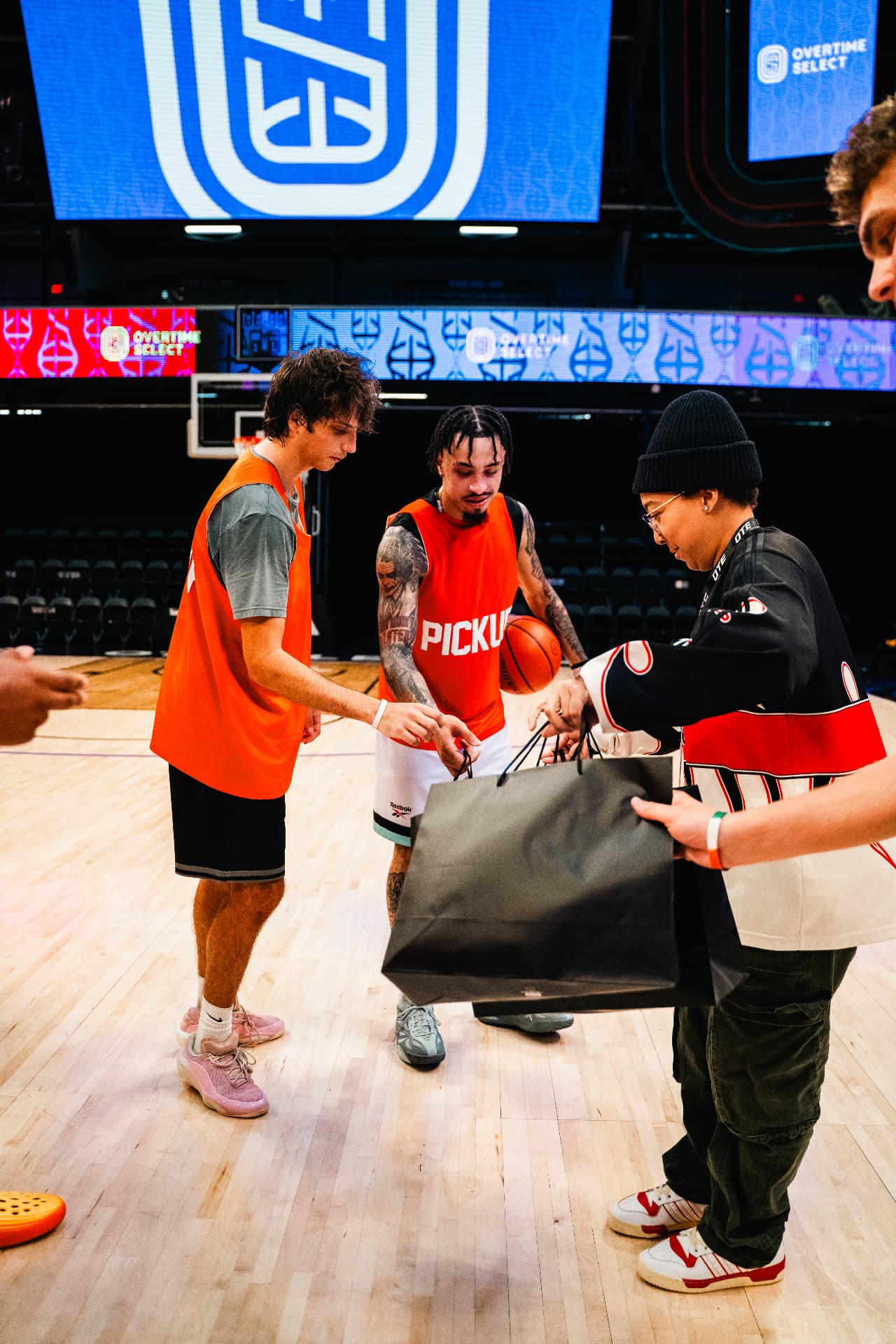 Hoopers in orange Pickup pinnies receiving black giveaway bags on an arena court